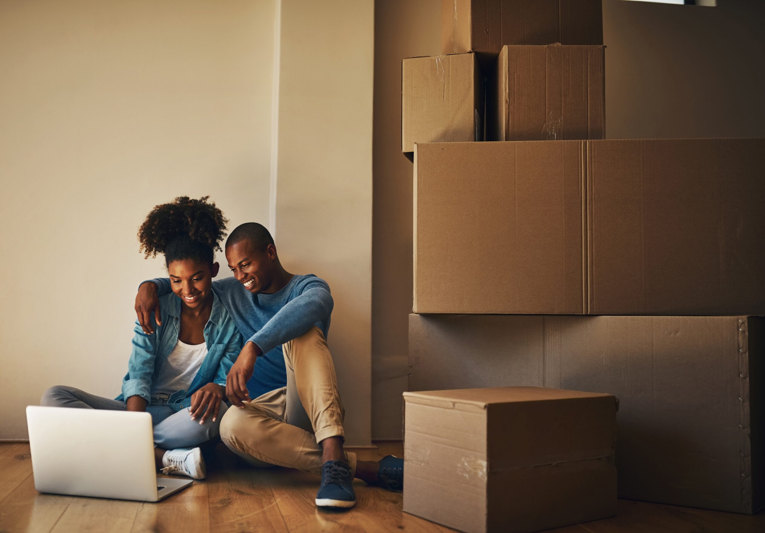 happy couple in new home sitting on the floor with a laptop