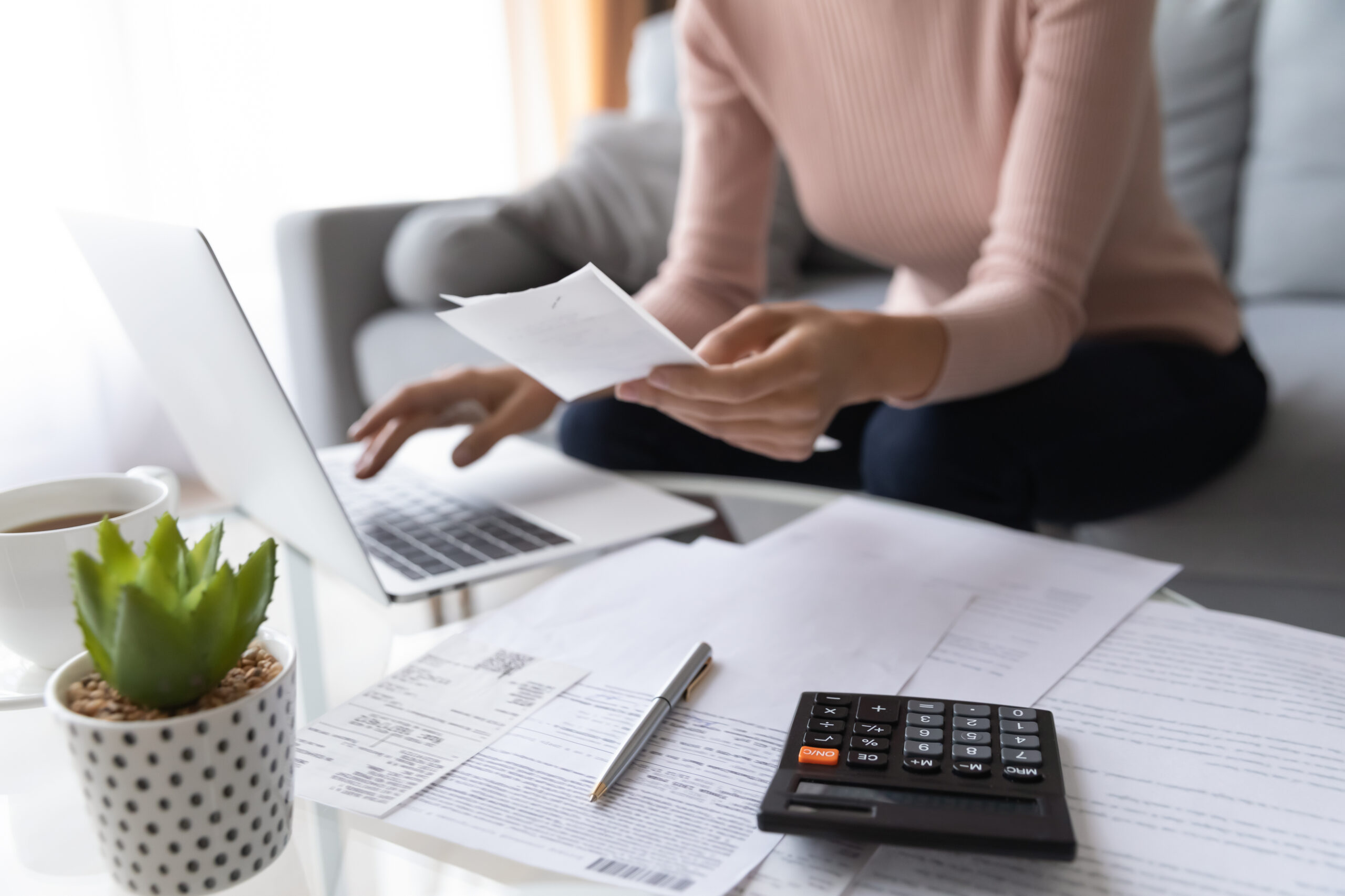 close up of woman working on laptop with paperwork and calculator