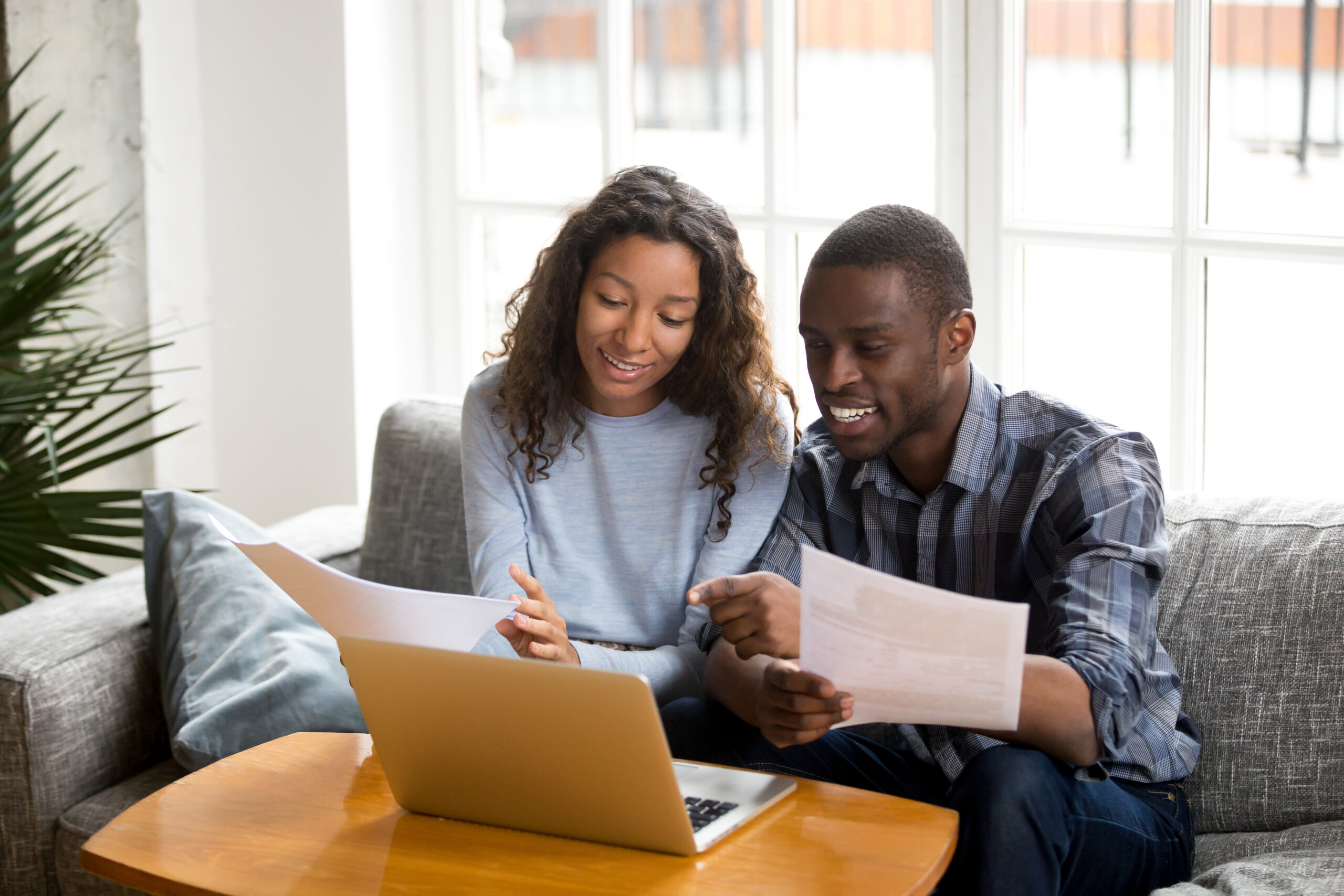 couple sitting on couch at home reviewing papers and with laptop open