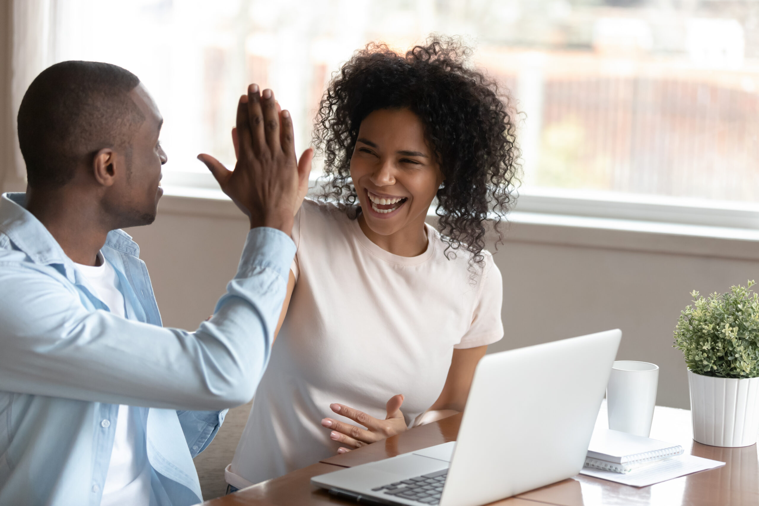 happy couple high fiving sitting at a table with a laptop