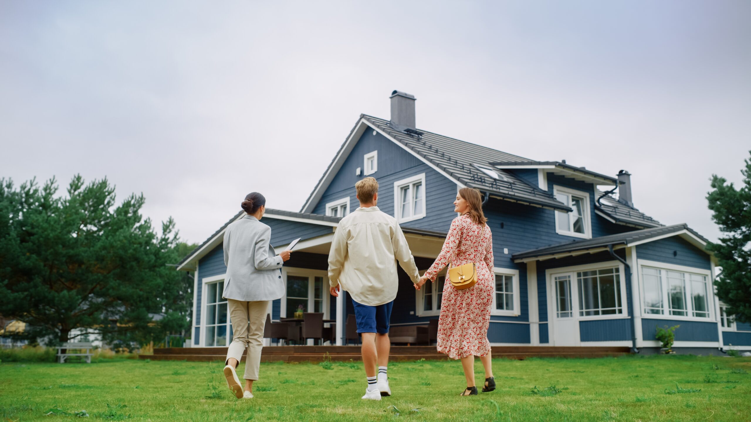 real estate agent showing a big blue home to young couple